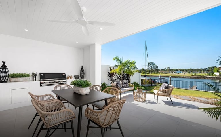 Modern outdoor living space with dining table, rattan chairs, and waterfront view overlooking landscaped grounds