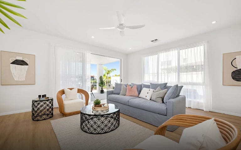 Modern bright living room with gray sofa, rattan chair, geometric coffee table, hardwood floors, and large windows with sheer curtains