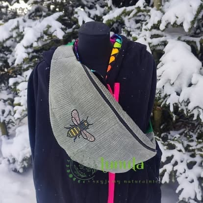 Mannequin wearing black jacket with colorful beaded necklace and light gray fabric bag with logo in snowy forest setting