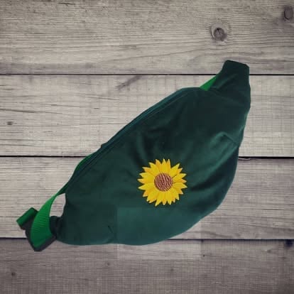 Green leaf-shaped pouch with yellow sunflower embroidery on wooden surface