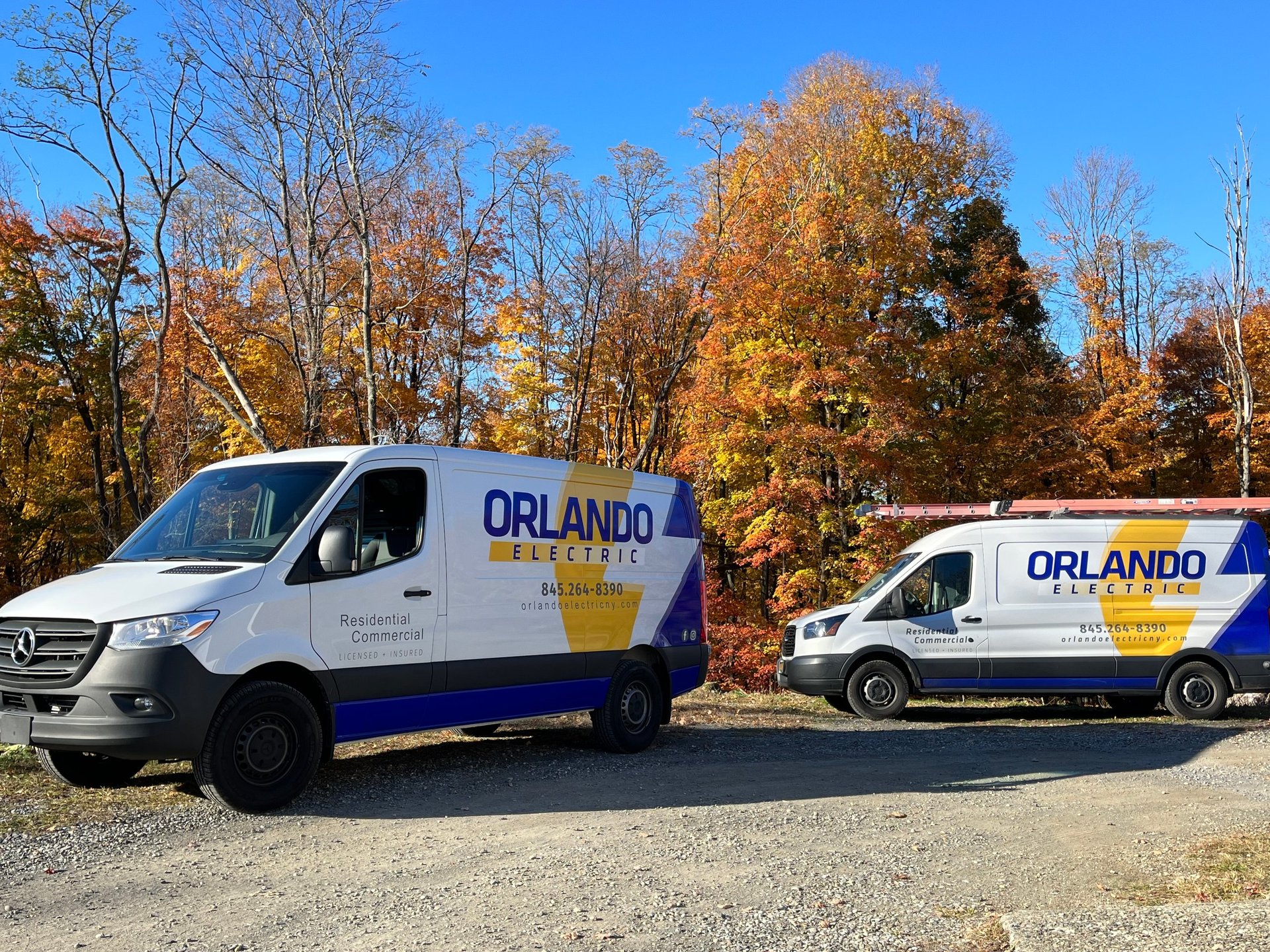 Two white Orlando Electric service vans parked side by side with autumn trees in the background