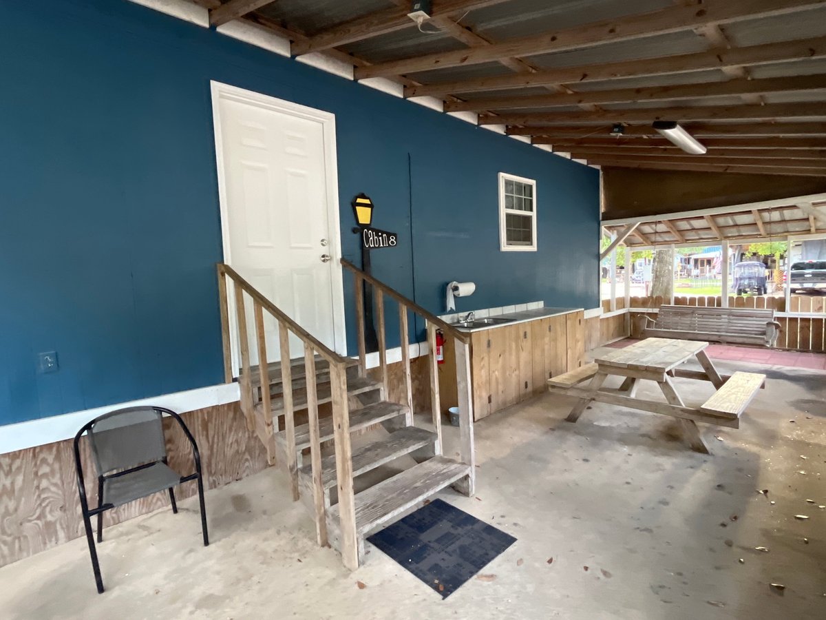 Blue cabin exterior with white door, windows, wooden ramp and stairs, picnic table on covered porch