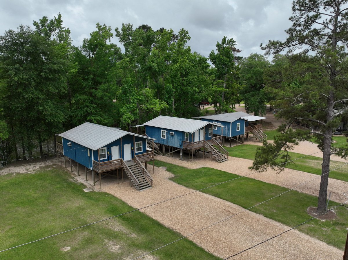 Aerial view of blue cabins on stilts with surrounding green lawn and trees