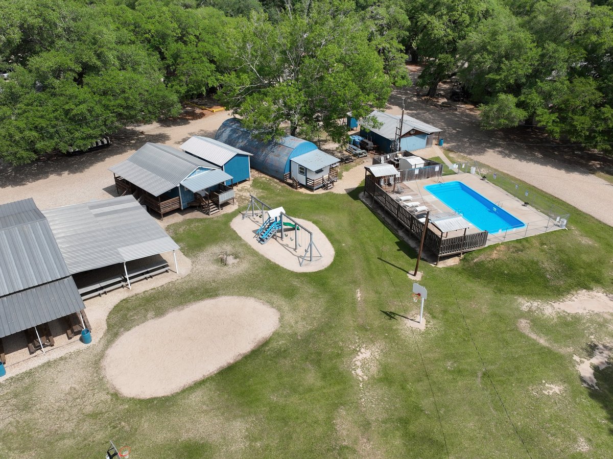 Aerial view of rural property with metal sheds, swimming pool, and playground