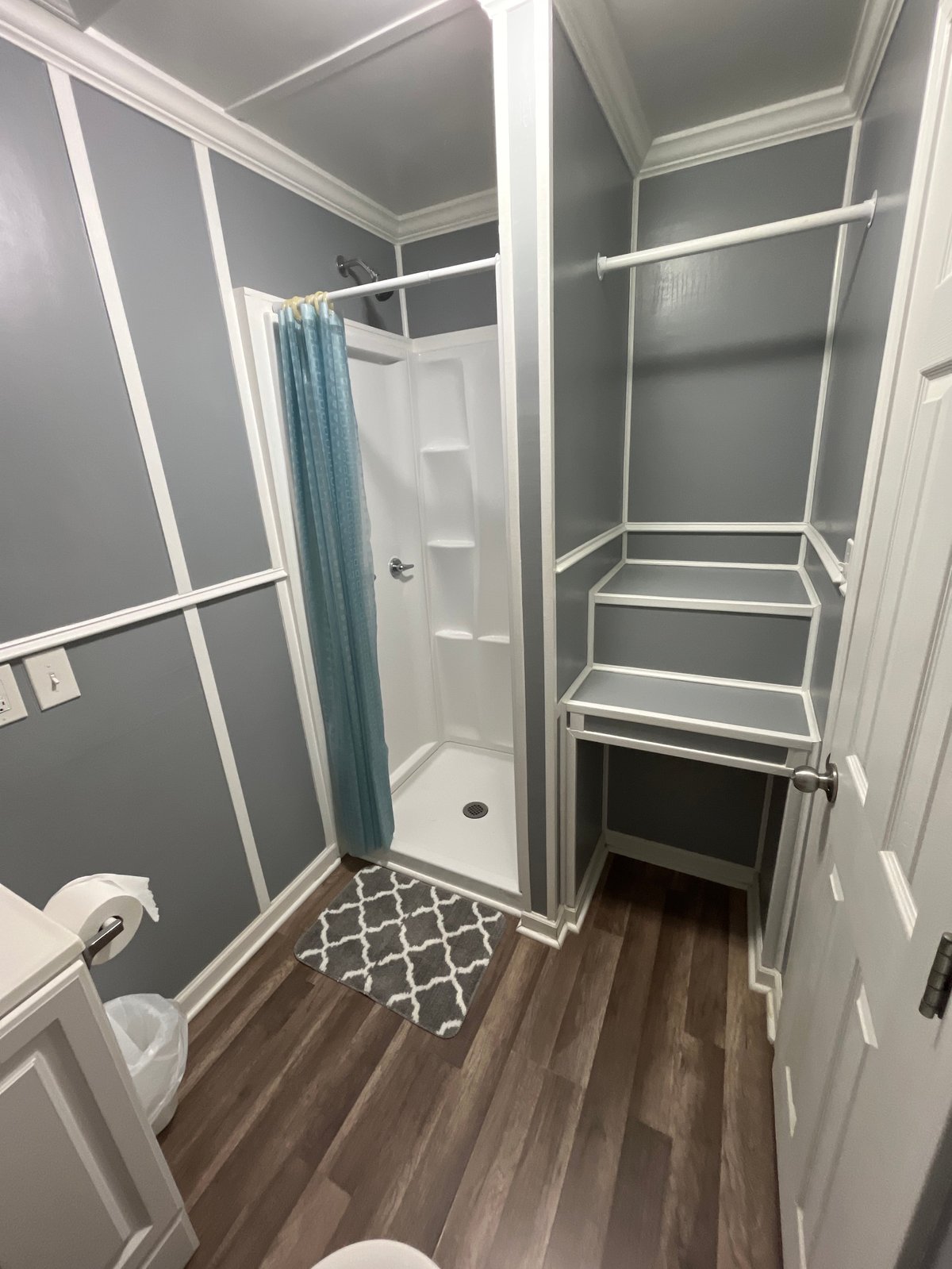 Cabin bathroom with walk-in shower, blue curtain, white shelving, and wood-grain flooring