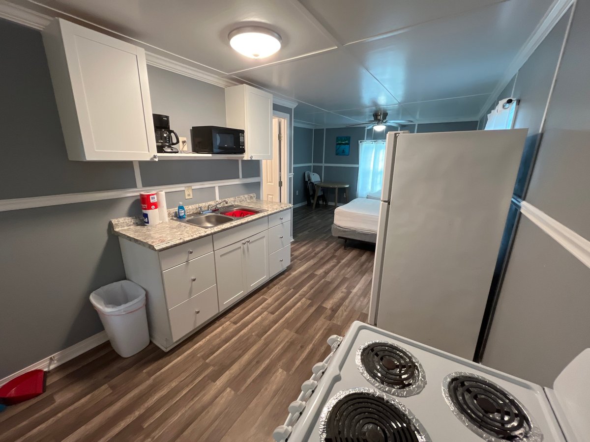 Cabin interior showing kitchen with white cabinets, stove, refrigerator, and living area