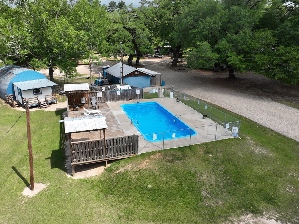 Aerial view of property with two blue swimming pools, wooden deck, and mature trees