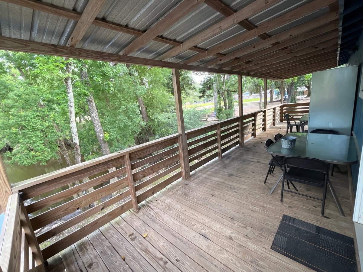 Wooden covered porch with horizontal railings, forest views, and outdoor furniture
