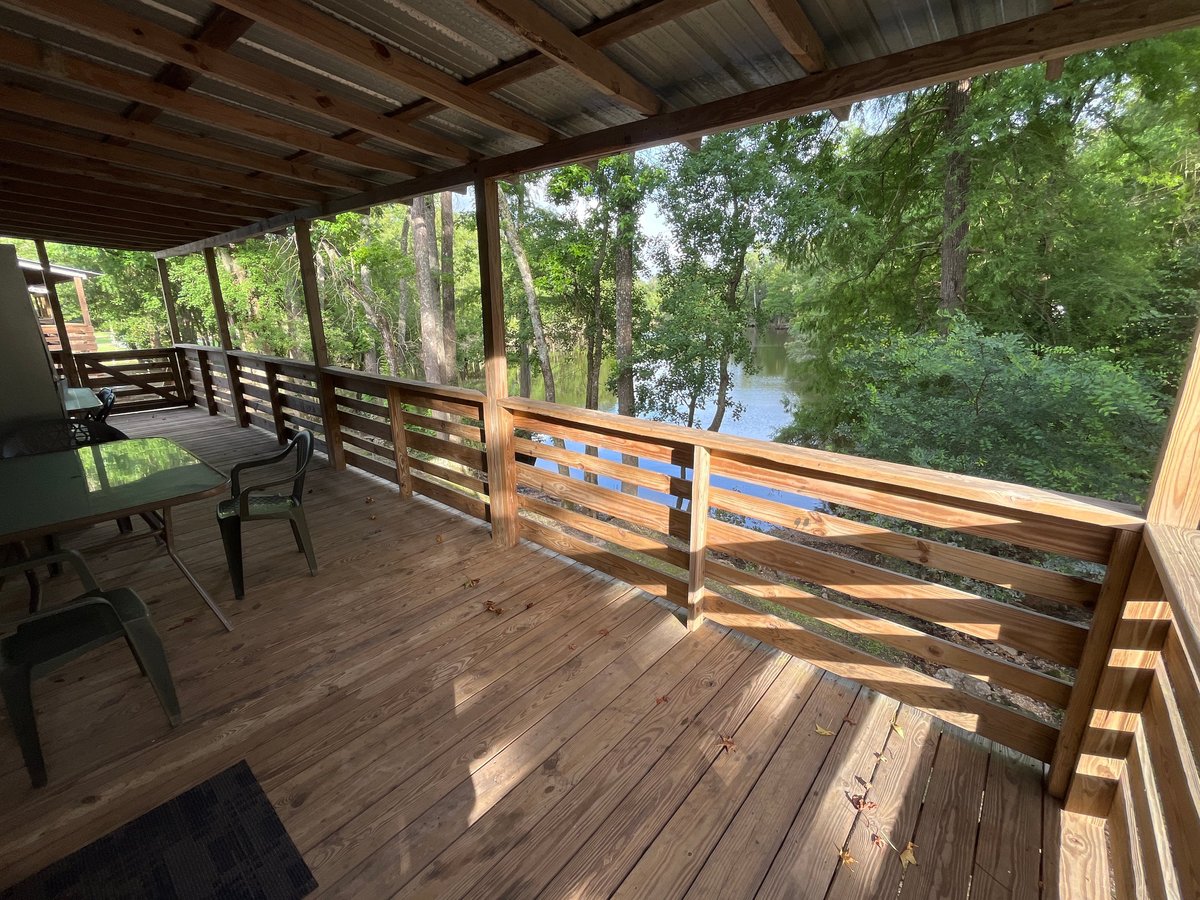 Covered wooden deck with rustic railing overlooking the Tangipahoa River and tree-lined landscape