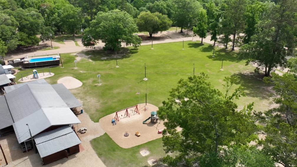 Aerial view of a park with playground, green lawn, mature trees, and covered pavilion structures