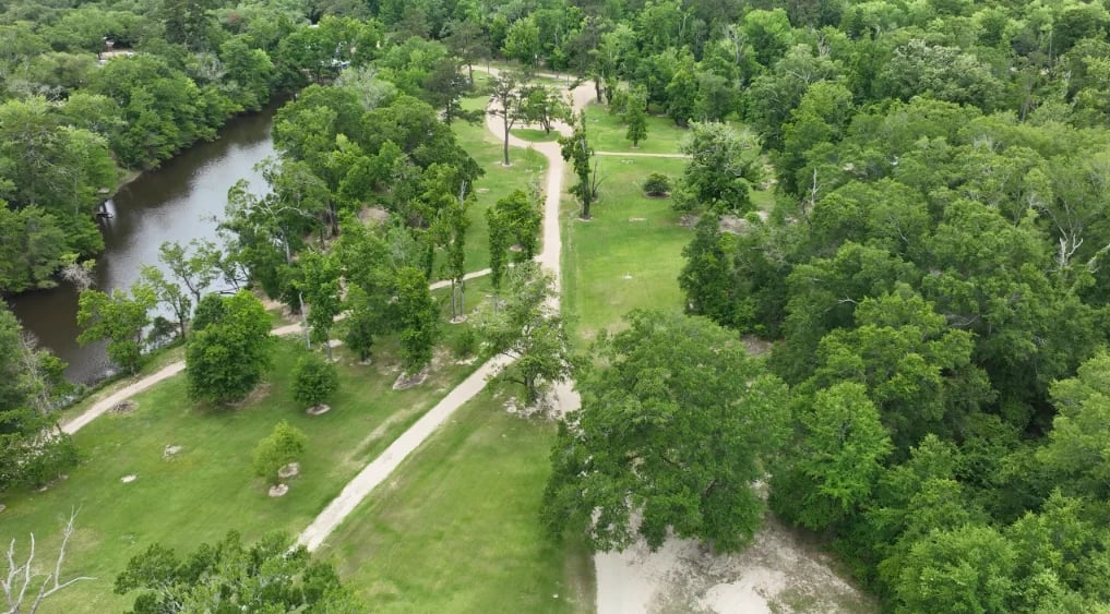 Aerial view of a lush green park with winding river, pathways, and trees