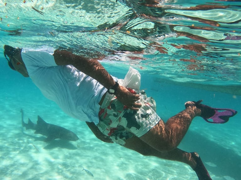 Snorkeler underwater in turquoise water wearing fins and snorkel gear with tropical fish visible below in Roatán