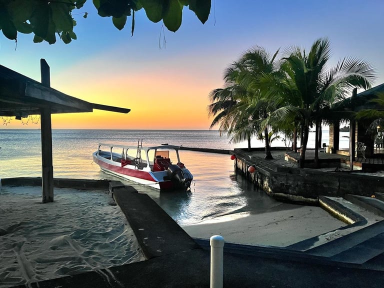 Wooden boat on a sandy beach at sunset with palm trees in West End, Roatán, Honduras