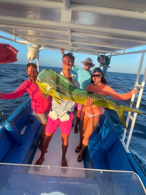 Group of anglers on a Roatán deep sea fishing charter displaying a large yellow and green mahi-mahi caught offshore in bright Caribbean sunlight