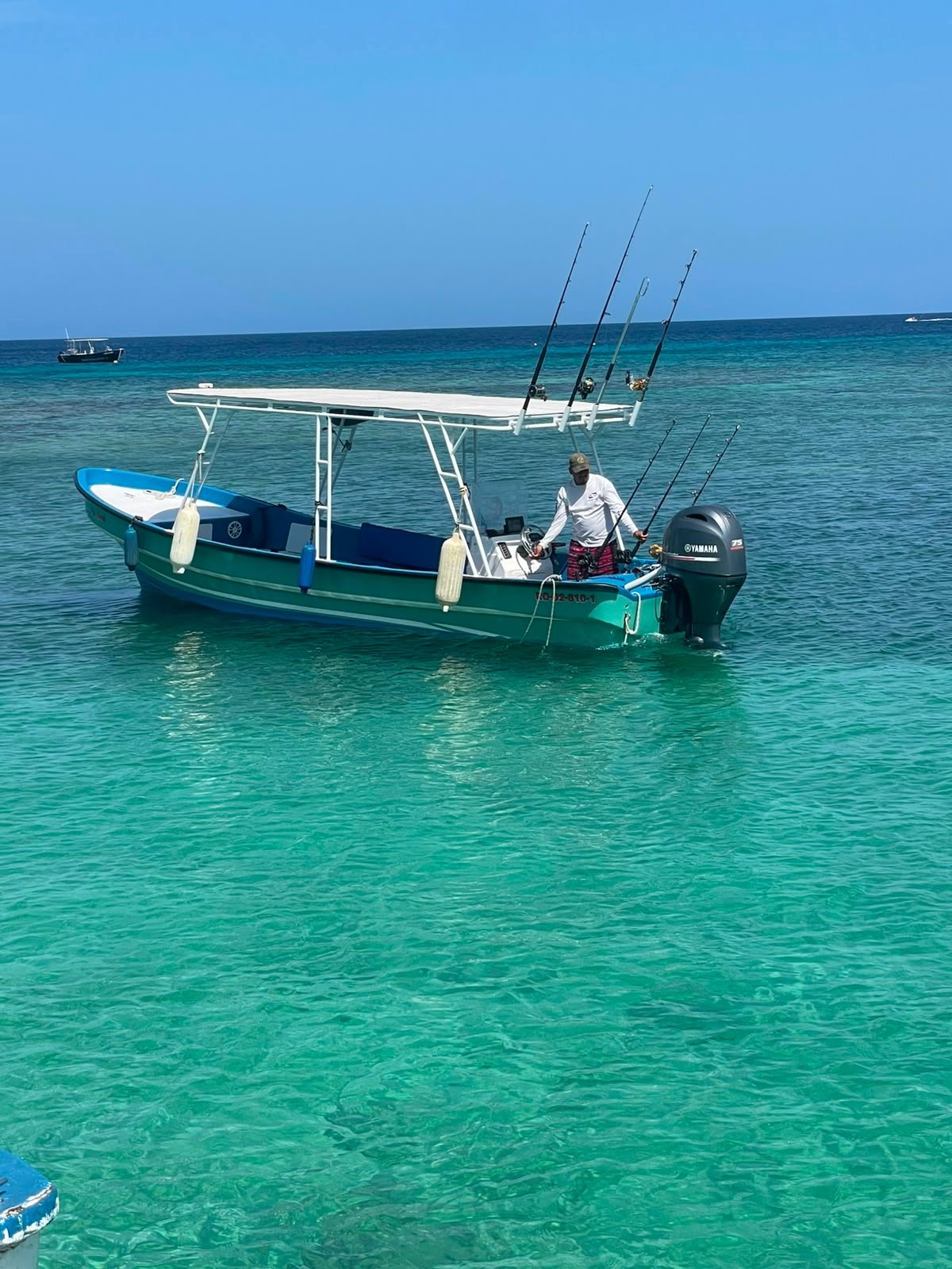 Green and white private fishing charter boat with tall trolling rods anchored in turquoise Caribbean water off Roatán, Honduras