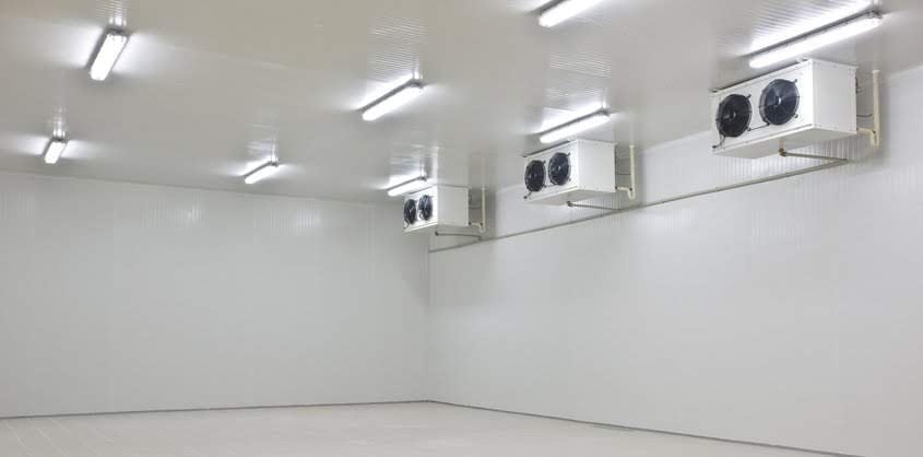 Cuarto frío industrial vacío con paredes blancas, luminarias fluorescentes y dos unidades de refrigeración montadas en techo