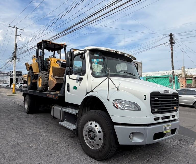 Plataforma de GRUPO MW transportando retroexcavadora amarilla