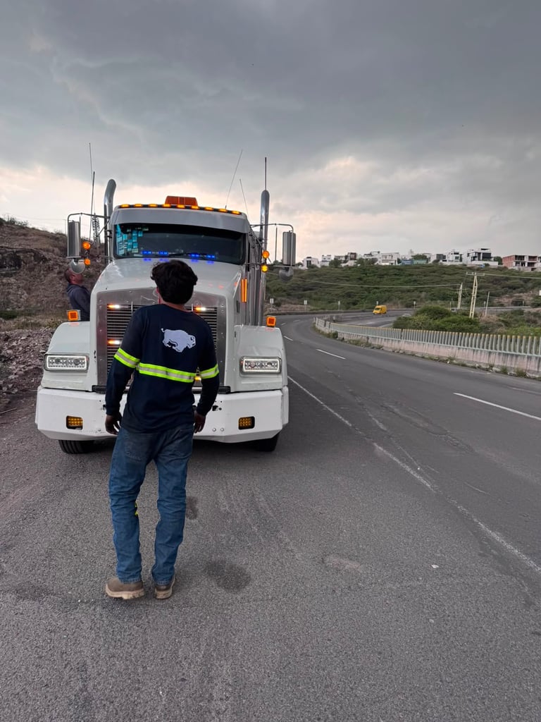 Worker in high-visibility vest standing in front of a large white semi truck on a highway