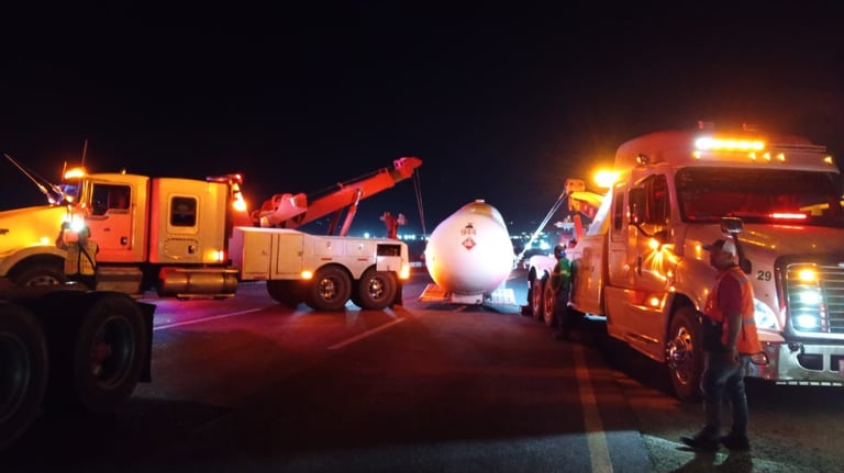 Escena nocturna con grúa, pipa de gas y bomberos en carretera