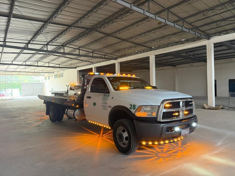 White and orange tow truck with amber warning lights in an industrial warehouse bay