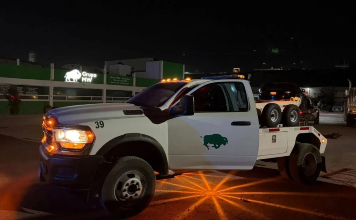 Pickup con luces de emergencia de noche en carretera con equipo pesado al fondo