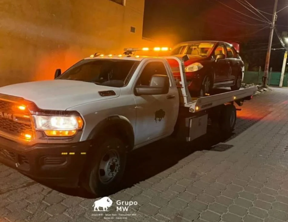 Grúa ligera GRUPO MW con plataforma trasladando vehículo rojo de noche