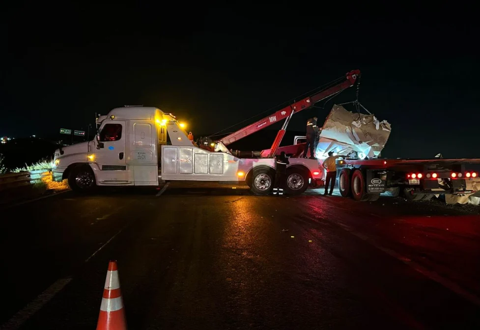 Grúa pesada MW levantando vehículo volcado de noche con conos de seguridad