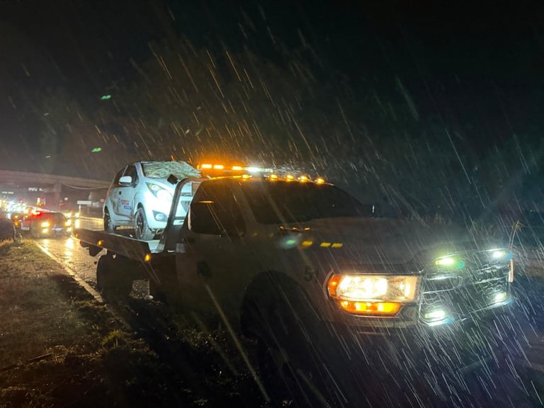 Tow truck hauling a white pickup truck on a rain-soaked highway at night with vehicles following behind