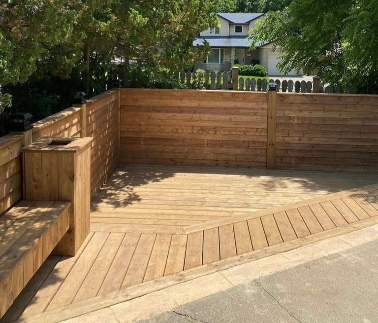 Wooden deck with horizontal wood fencing in a residential backyard, with green trees and a house visible in the background