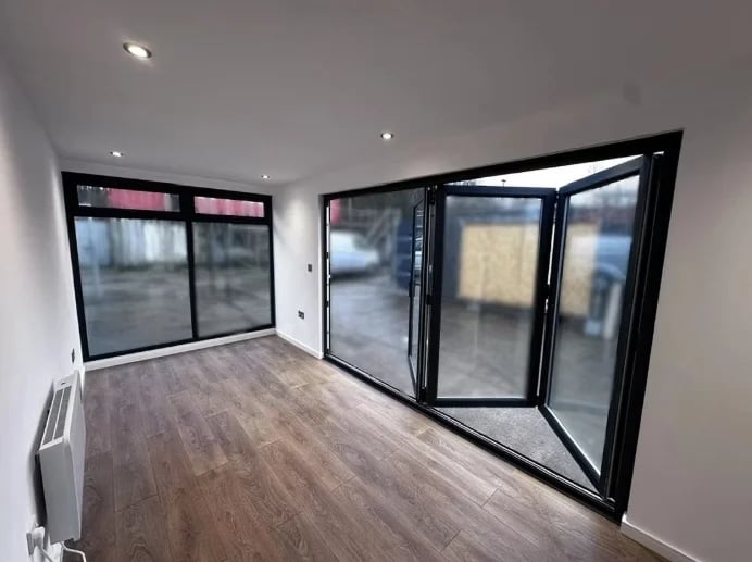 Empty modern apartment interior with large black-framed windows and glass doors, wooden flooring, and white walls