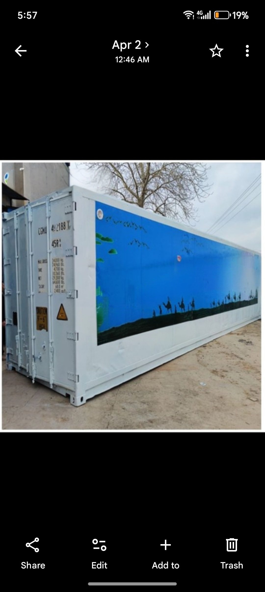 White and blue shipping container with pixelated retro video game art on sandy ground outdoors