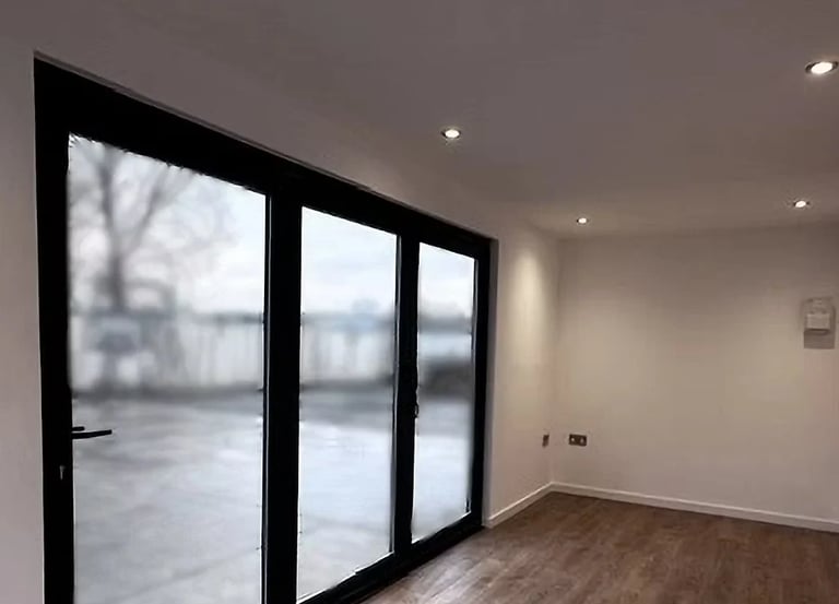 Modern room with large black-framed sliding glass doors opening to outdoor patio, recessed lighting, and wooden flooring
