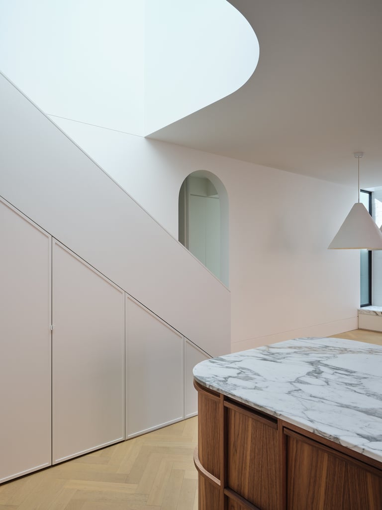 Modern minimalist interior with curved white walls, a marble-topped wooden counter, and an arched window with hanging pendant light