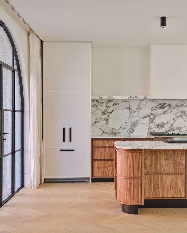 Modern kitchen with cream cabinetry, wood curved island with marble countertop, and black-framed glass door