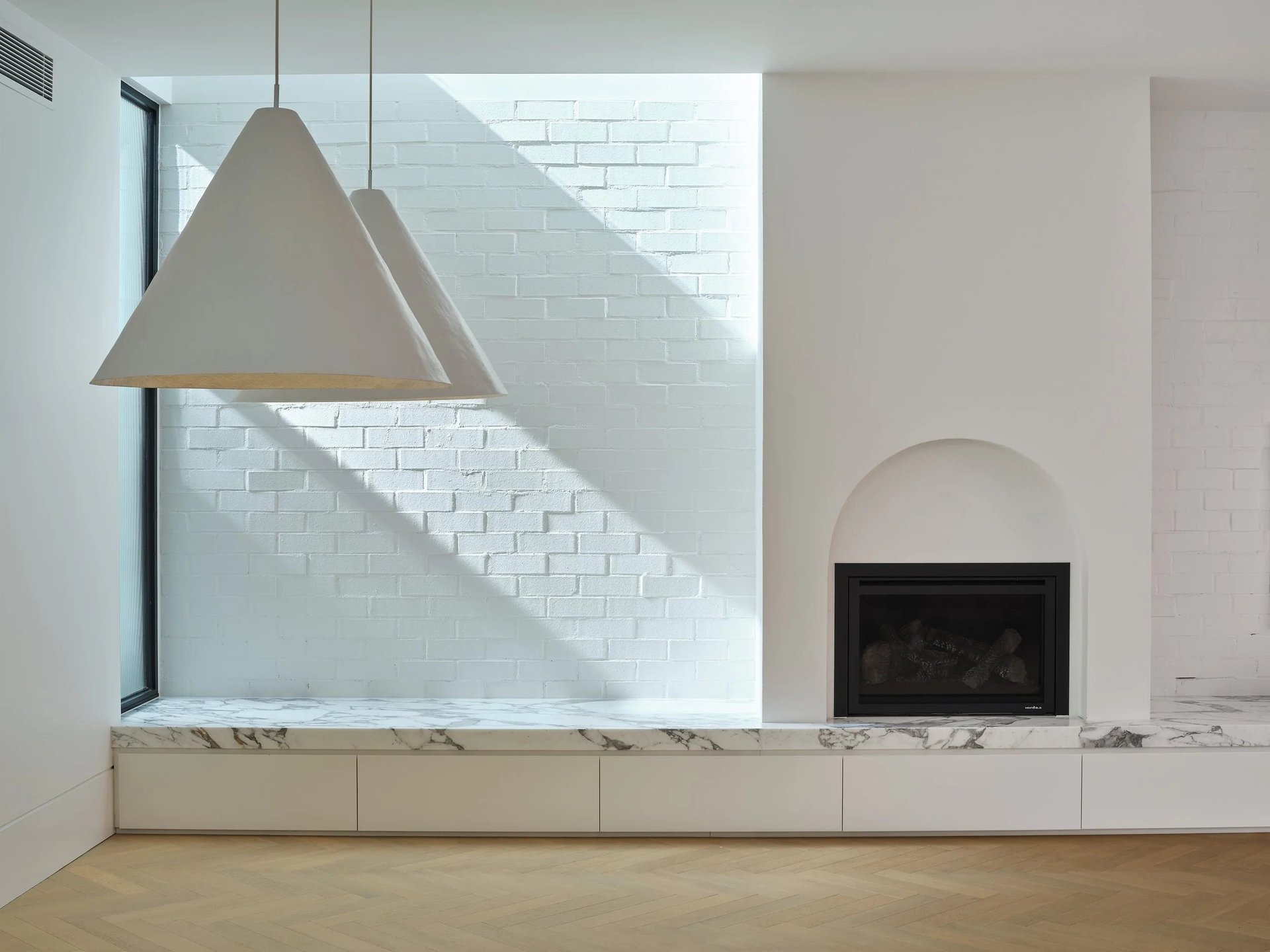 Modern minimalist interior with a geometric concrete pendant light, white subway tile wall, arched fireplace, and marble-topped built-in bench seating