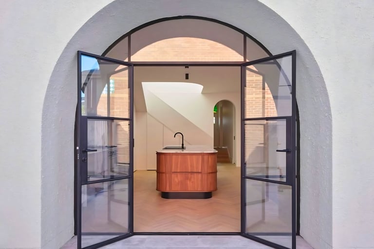 Modern bathroom viewed through open black-framed glass doors with wooden sink basin and arched ceiling