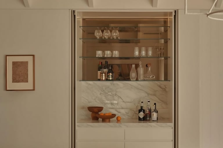 Built-in display cabinet with marble base and wood shelving containing glassware, bottles, and decorative bowls in a modern living room