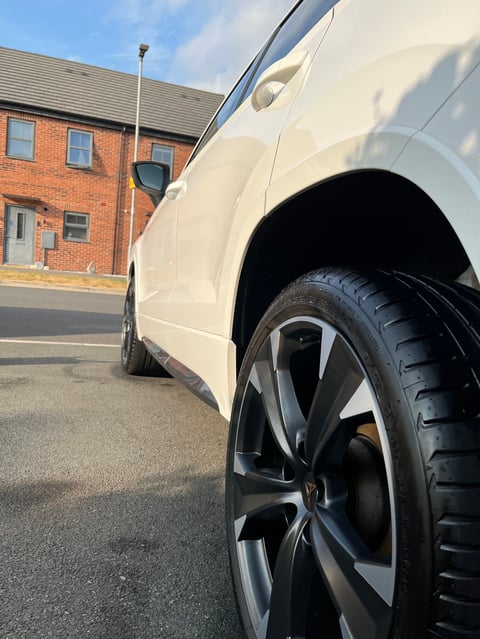Close-up of a white vehicle's side and wheel parked in front of a brick house