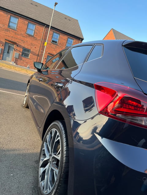 Two cars parked nose-to-nose in a driveway beside a brick house on a sunny day