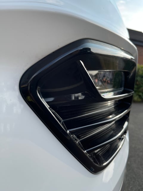 Close-up of a black sleek car side mirror mounted on white vehicle body with chrome trim detail