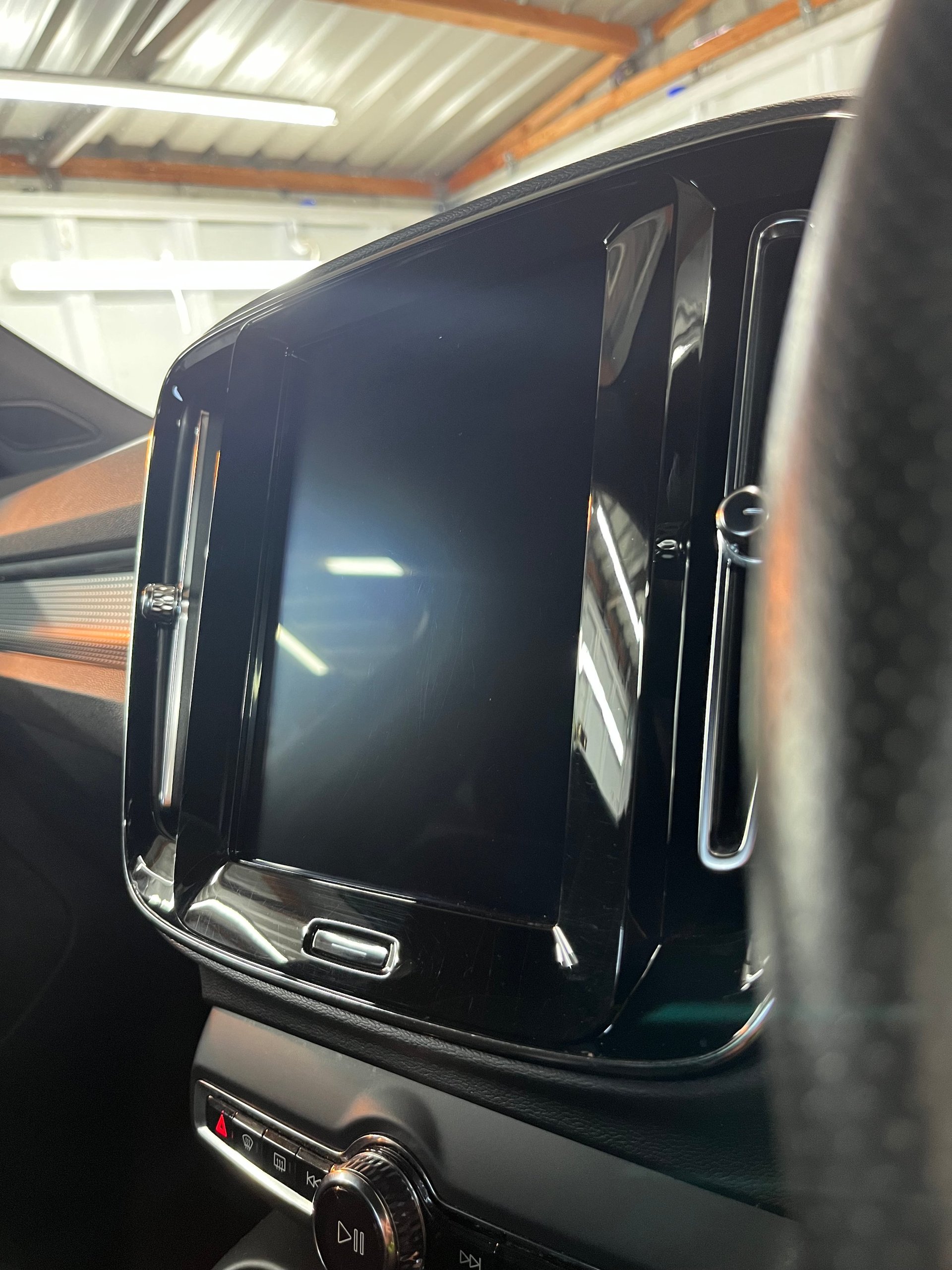 Black car door with chrome trim open in a garage workshop with corrugated metal roof and wooden beams