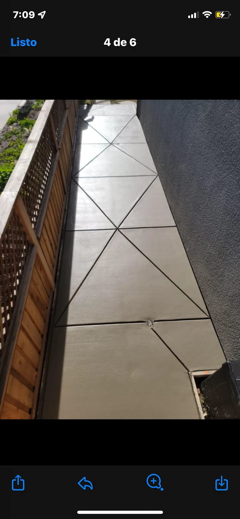 Narrow diagonal-pattern concrete walkway between wooden fence and gray wall