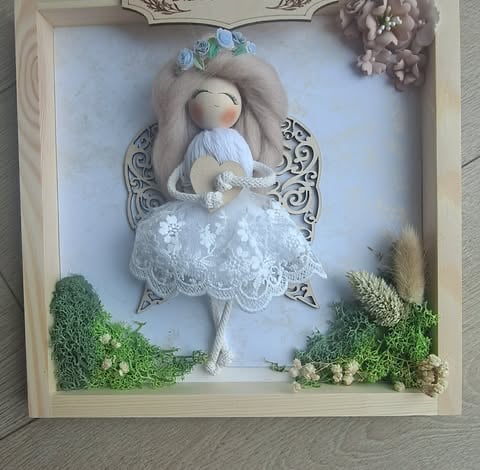 Handmade angel doll with white lace dress and flowers in decorative wooden frame with moss and foliage