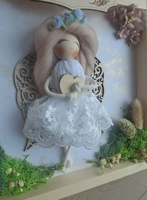 Handmade fabric angel doll with gray hair, blue flower crown, white lace dress, and decorative wings displayed on a shelf with moss and dried flowers