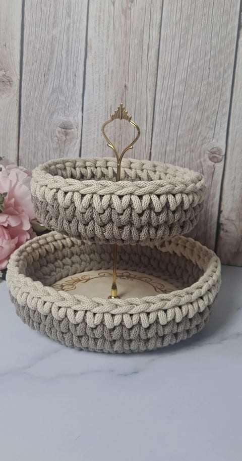 Two-tier cream knitted basket with brass holder and pink flowers on weathered white wooden background