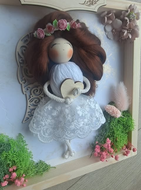 Handmade fabric doll with brown hair, pink flower crown, and white lace dress displayed in a decorative frame with moss and pink flowers