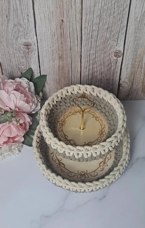 Cream-colored rope tiered candle holder with ornate gold design next to pink peonies on white marble surface against rustic wood backdrop