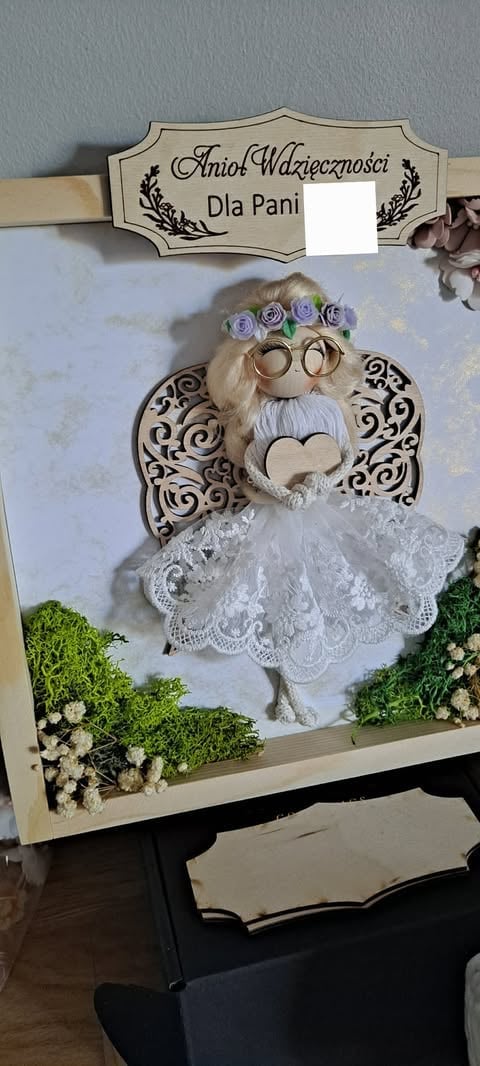 Handmade decorative angel figurine with white beard, purple flower crown, lace wings, and glasses in a wooden frame with green moss and flowers