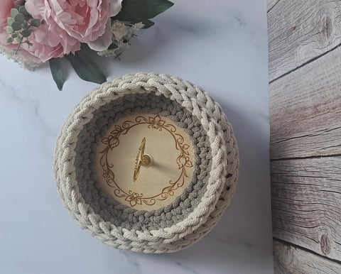 Rope-wrapped round wall clock with gold accents on marble surface next to pink roses and wooden flooring
