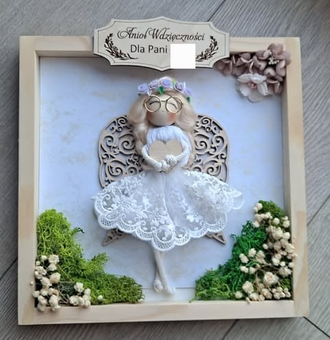 Decorative wooden frame with handmade angel figurine wearing white lace dress, glasses, and flower crown, surrounded by moss and white flowers
